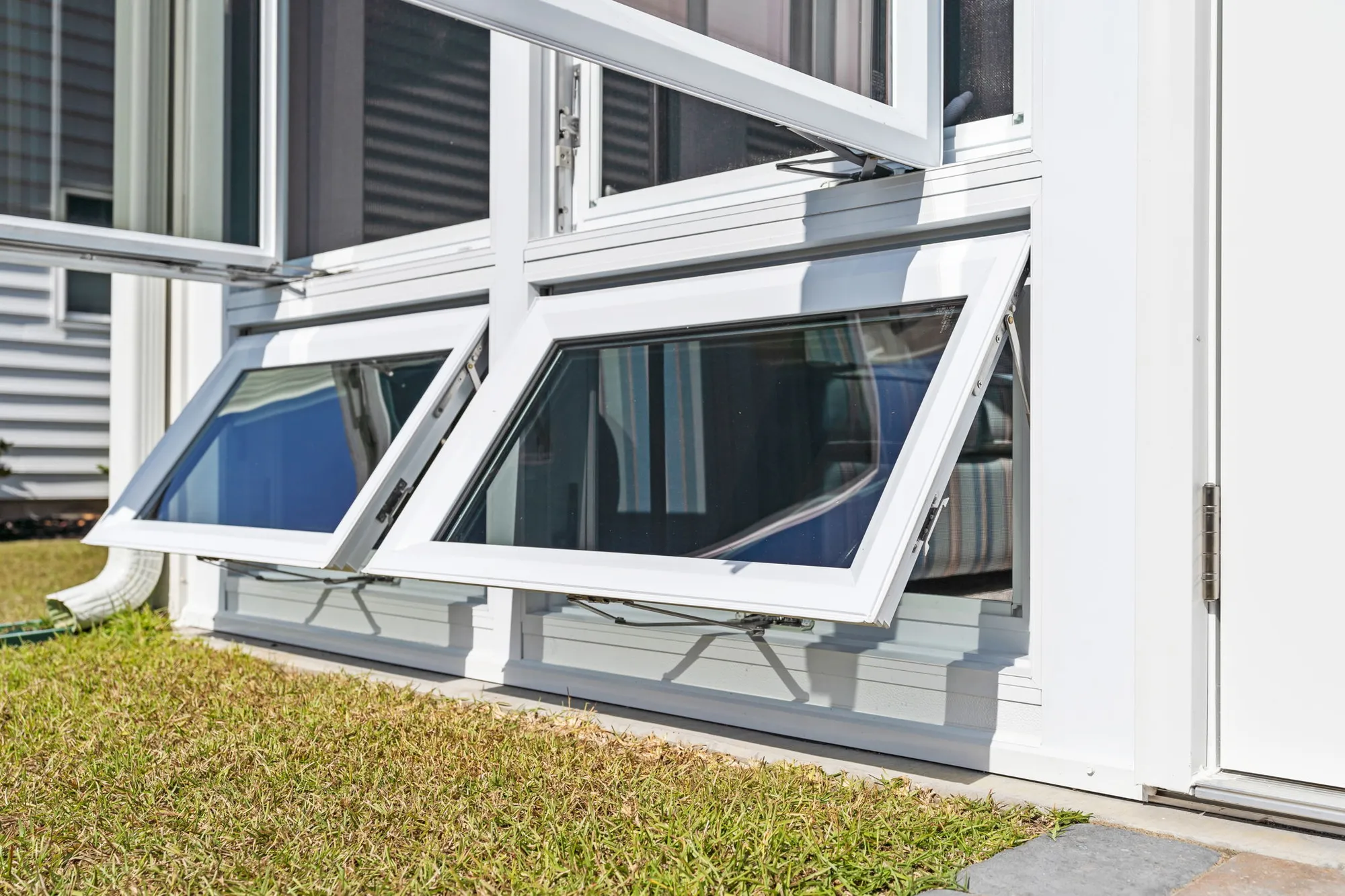 Close-up of white awning-style basement windows open outward, allowing ventilation and natural light into a lower-level room