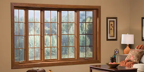 A cozy living room featuring large wood-framed bay windows overlooking greenery, showcasing elegant bay window decorating ideas that enhance warmth and natural light