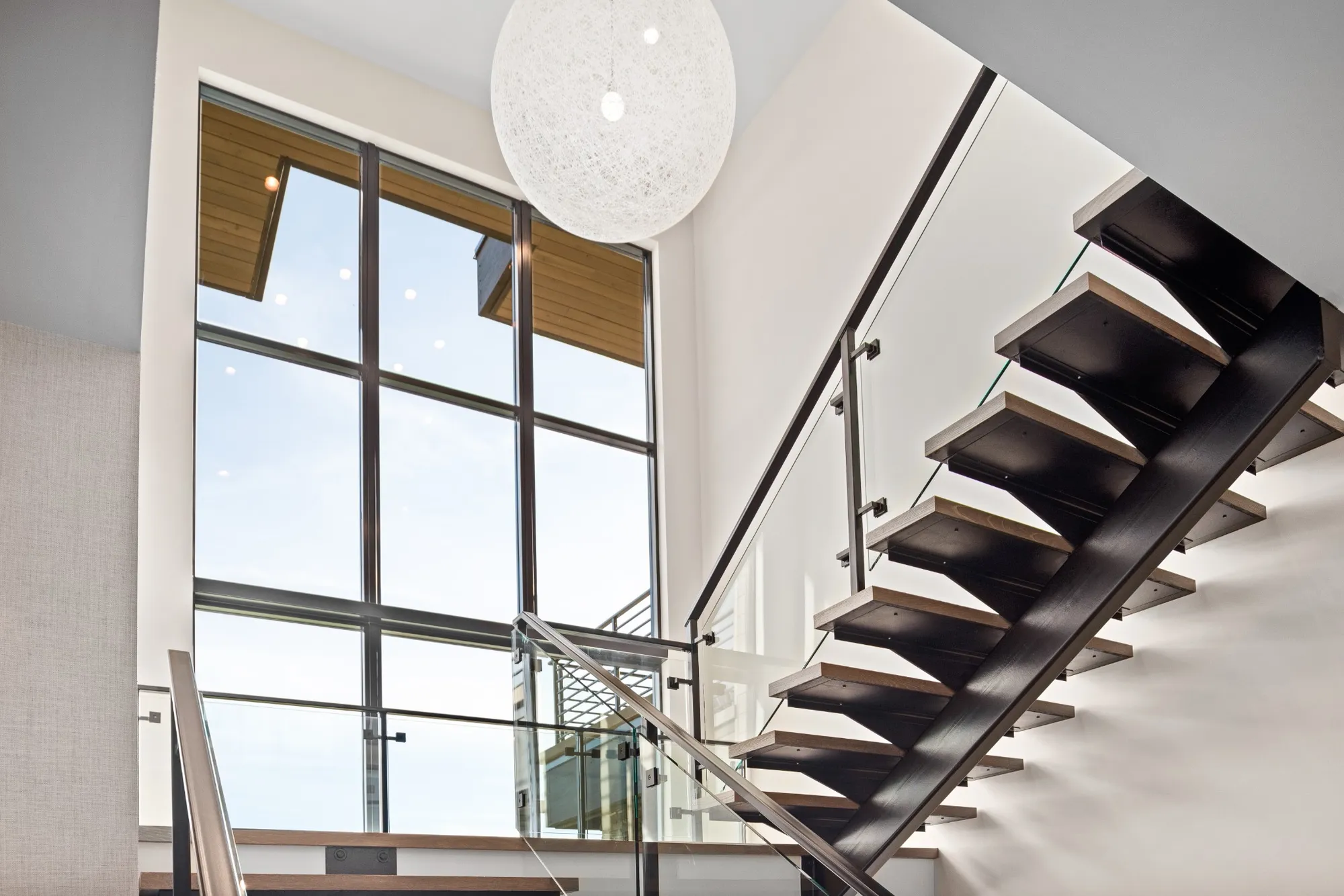 Modern interior with large windows enhancing natural light home design, featuring a sleek glass staircase and minimalist architectural details