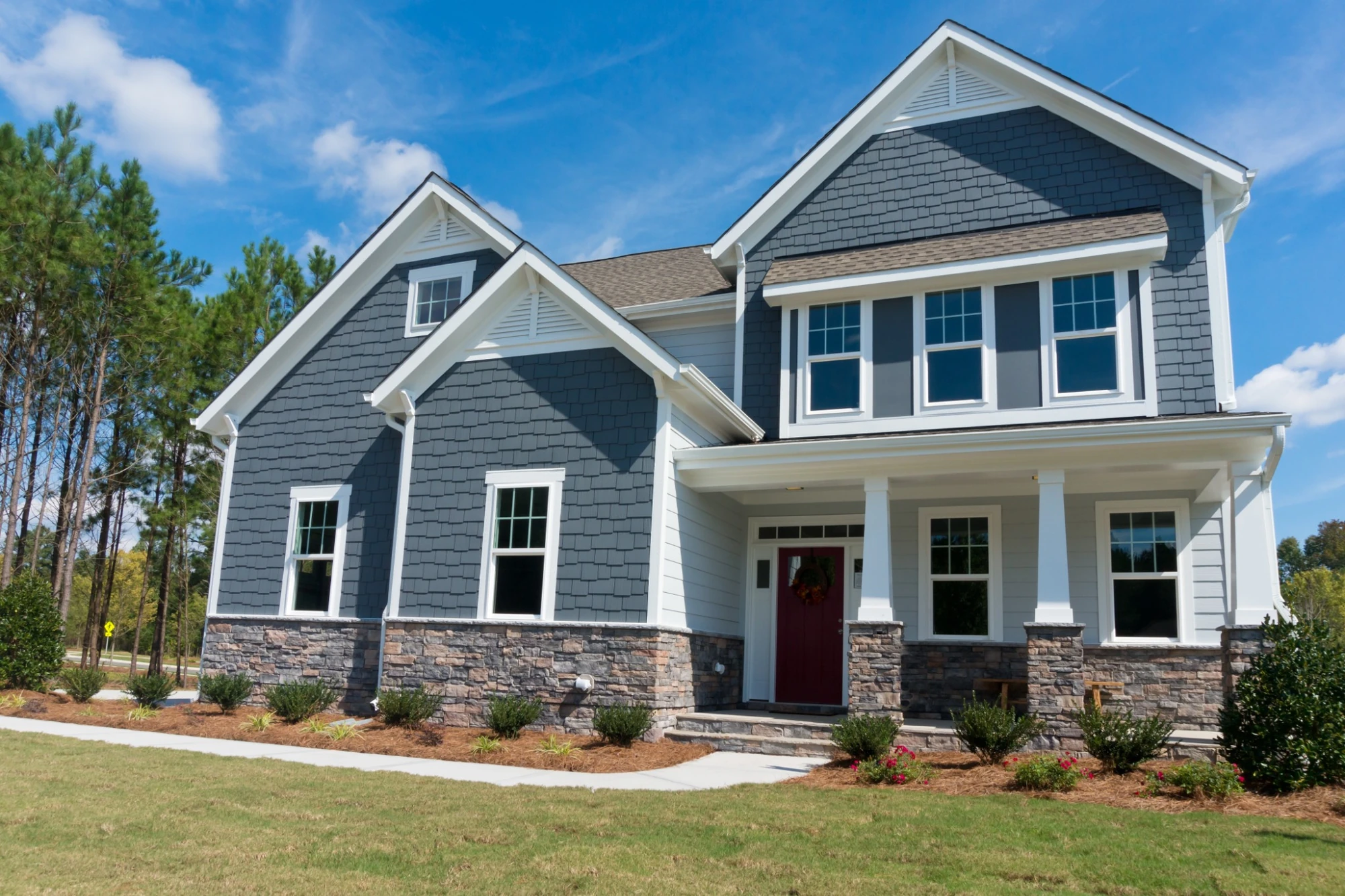 Exterior of a modern two-story home with updated basement window replacement, featuring white-framed windows and stone foundation accents