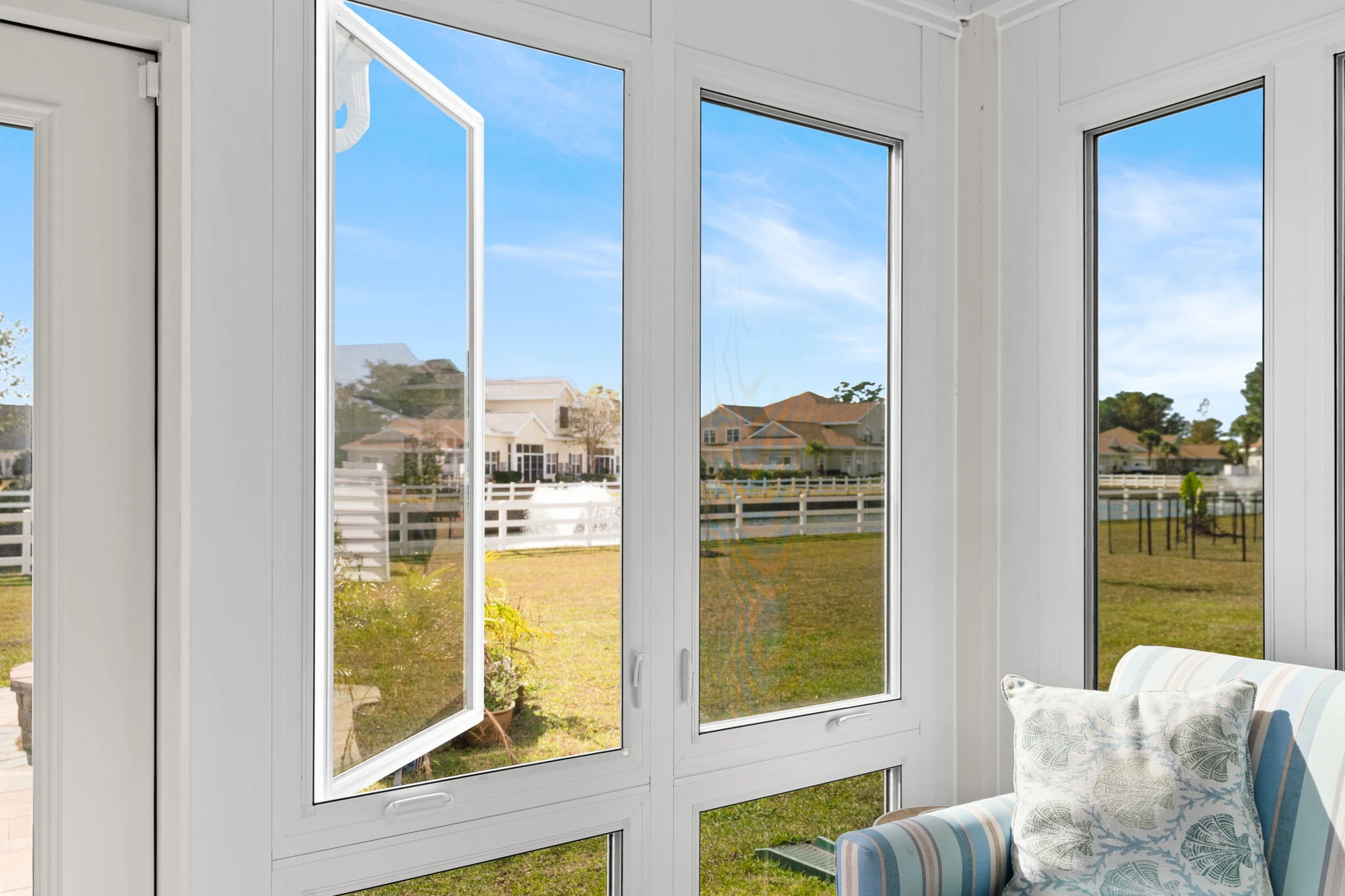 Open white casement-style basement windows letting in natural light and fresh air, with a view of a landscaped backyard