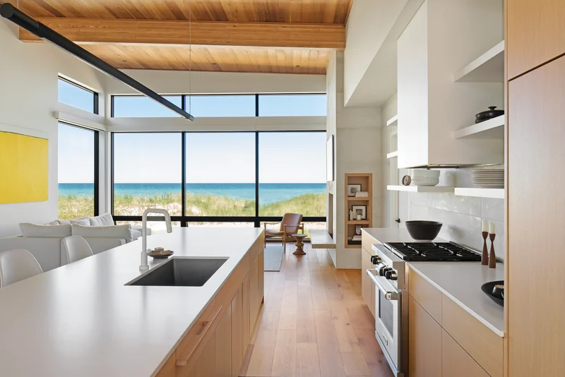 Image of window replacement cost example — modern floor-to-ceiling black frame windows with ocean view in open kitchen