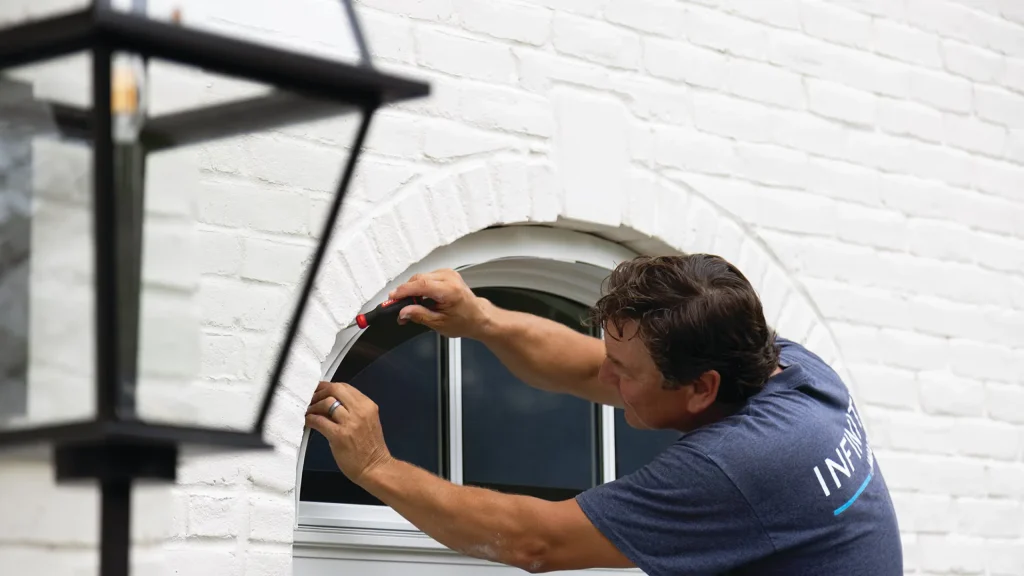 Image of a professional installer fitting a specialty arched window into a white brick home exterior