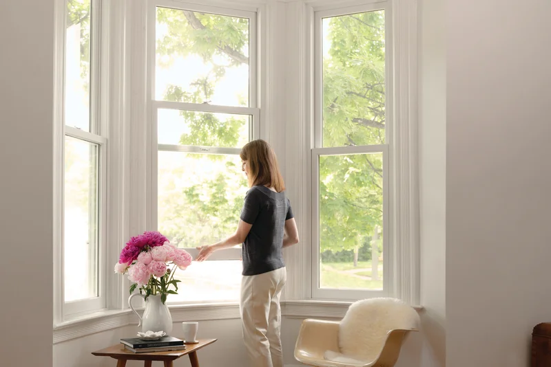 Image of a homeowner looking out bright replacement windows in a sunlit living room