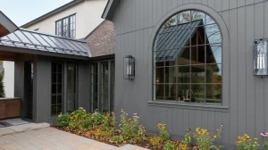 Image of a gray modern home exterior with a large arched window and standing seam metal roof accent