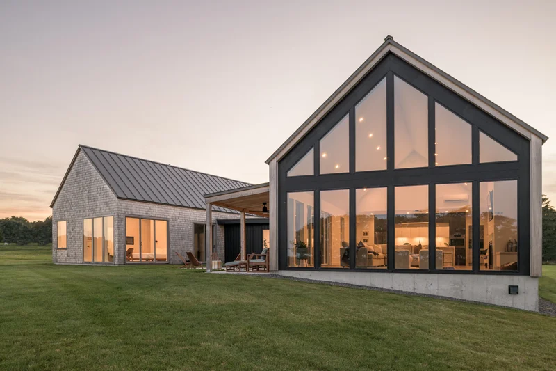Image of a modern farmhouse exterior with large black-framed windows at dusk